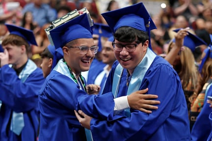 two graduating students in blue gowns hugging and celebrating